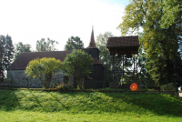 Duży kamienny kościół wśród drzew z drewnianą wieżą, po prawej stronie dzwonnica